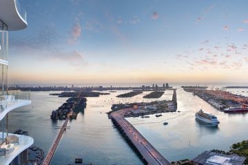Balcony of a modern apartment with glass railing, overlooking a harbor at sunset.