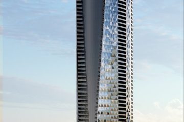 Tall curved glass skyscraper by the ocean, with a landscaped foreground and palm trees along the street.