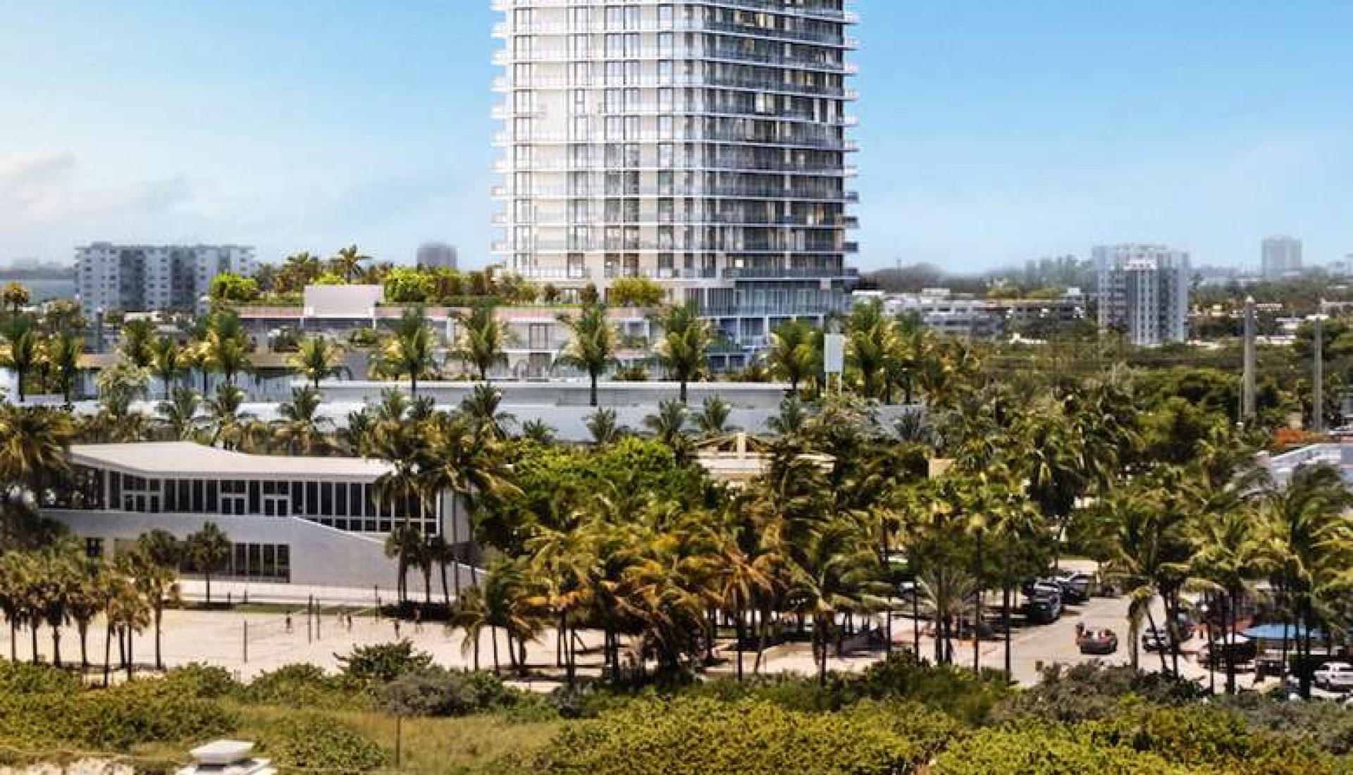 Tall glass hotel tower overlooks a sunny beach with palm trees and rows of lounge chairs on white sand.