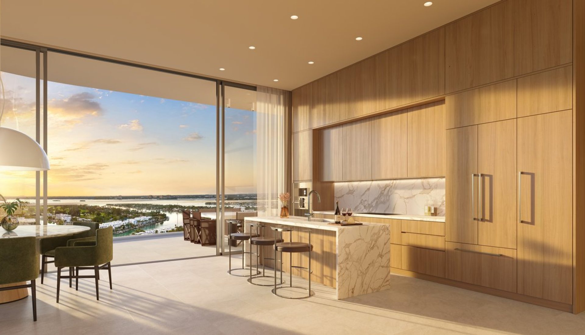 Modern kitchen with wooden cabinets and a marble island, overlooking a sunset harbor through large glass doors.