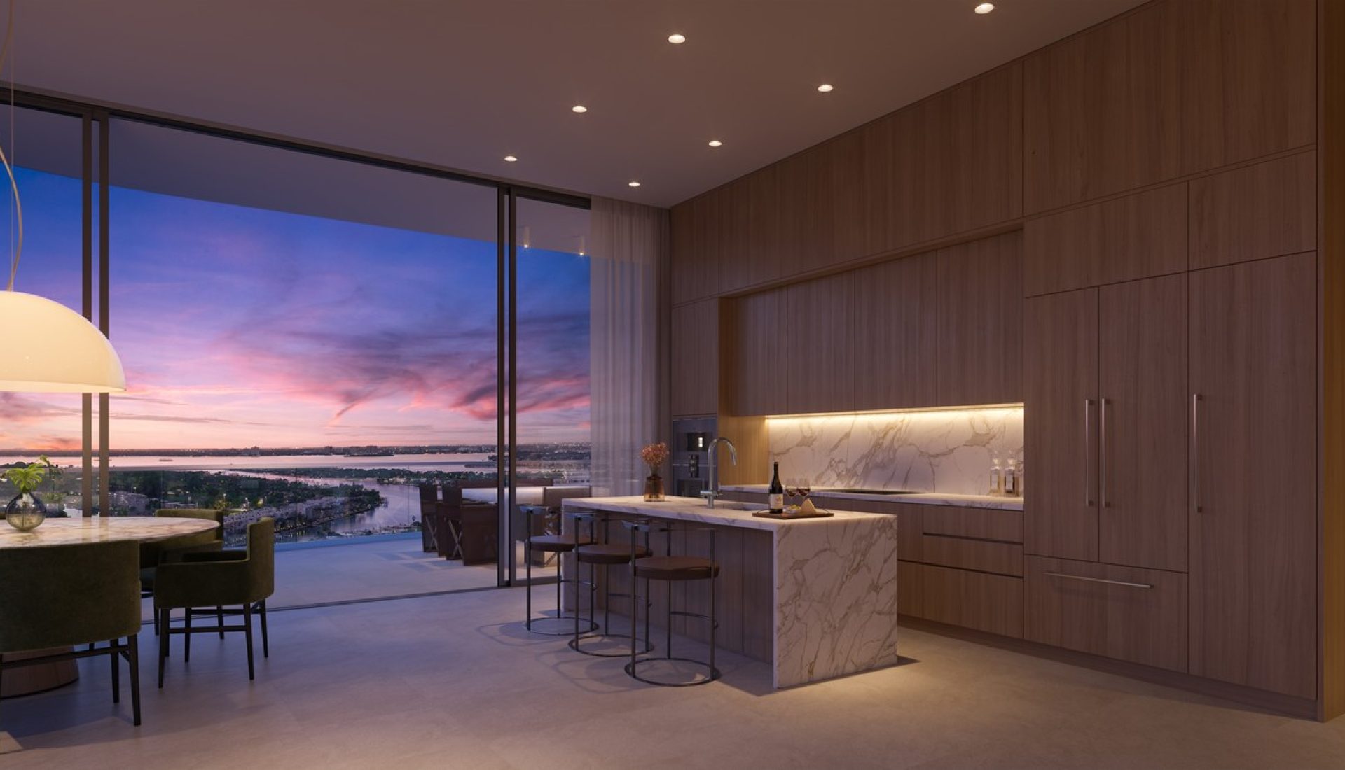 Modern open-plan kitchen with a marble island and wooden cabinets, overlooking a sunset balcony view.