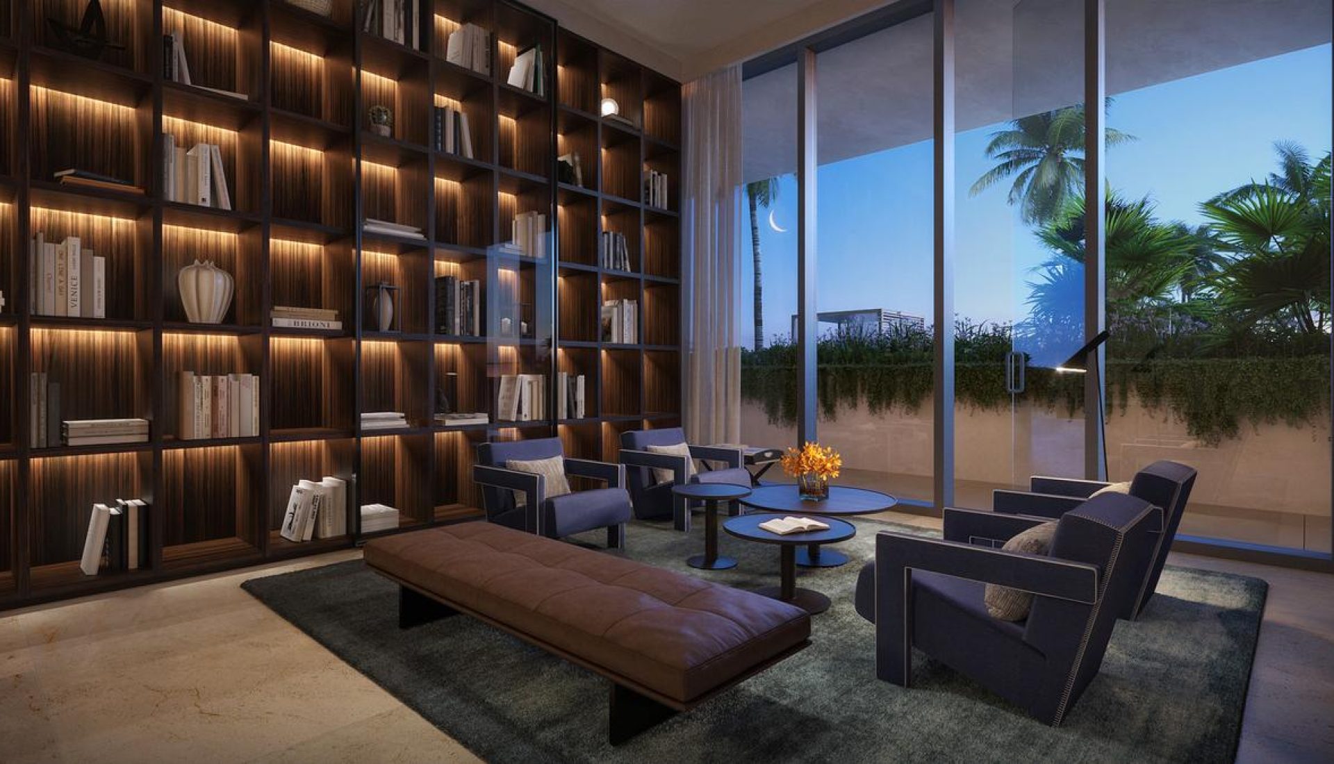 Elegant library lounge with floor-to-ceiling illuminated bookshelves, a brown leather bench, and blue armchairs around small tables beside glass doors opening to a night garden.