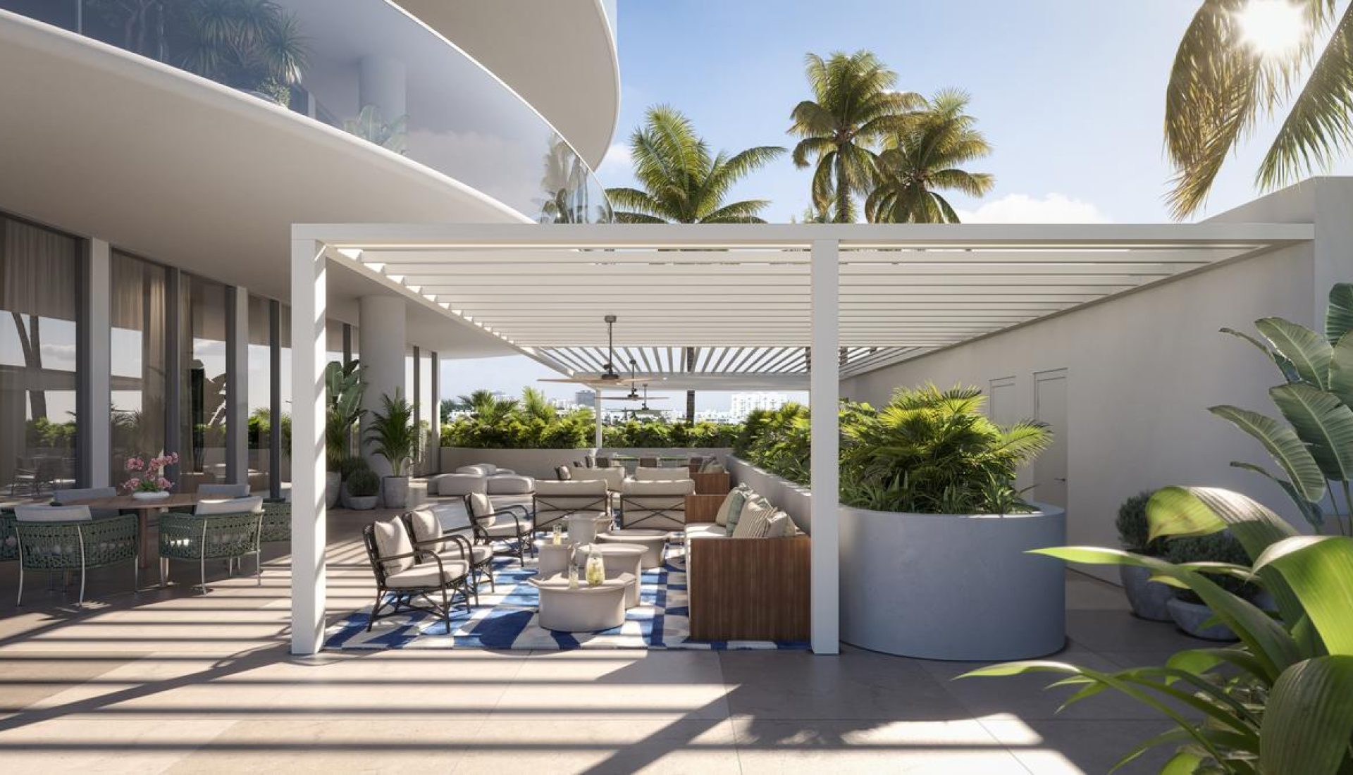 Modern rooftop lounge with a white pergola, comfortable seating, and a blue-and-white rug amid lush tropical plants.