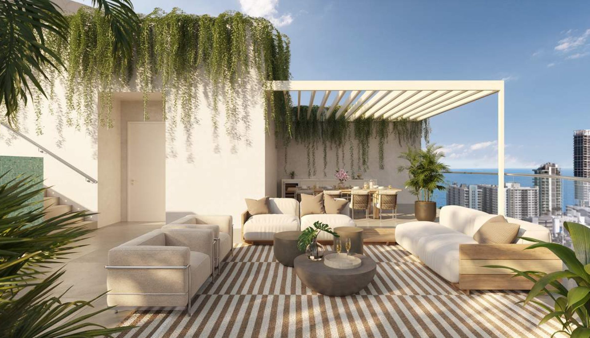 Luxurious rooftop lounge with beige couches, striped rug, and potted plants overlooking a city skyline and the ocean on a sunny day