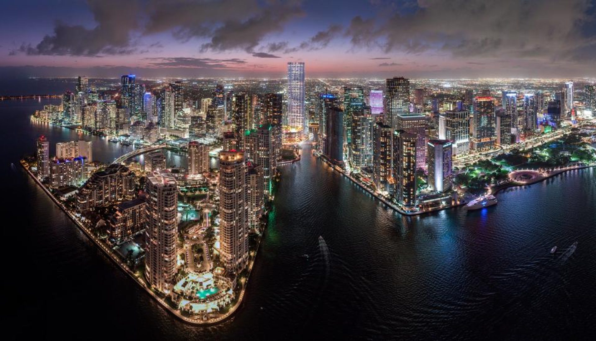 Aerial night view of a lit city skyline along a winding waterway and harbor.