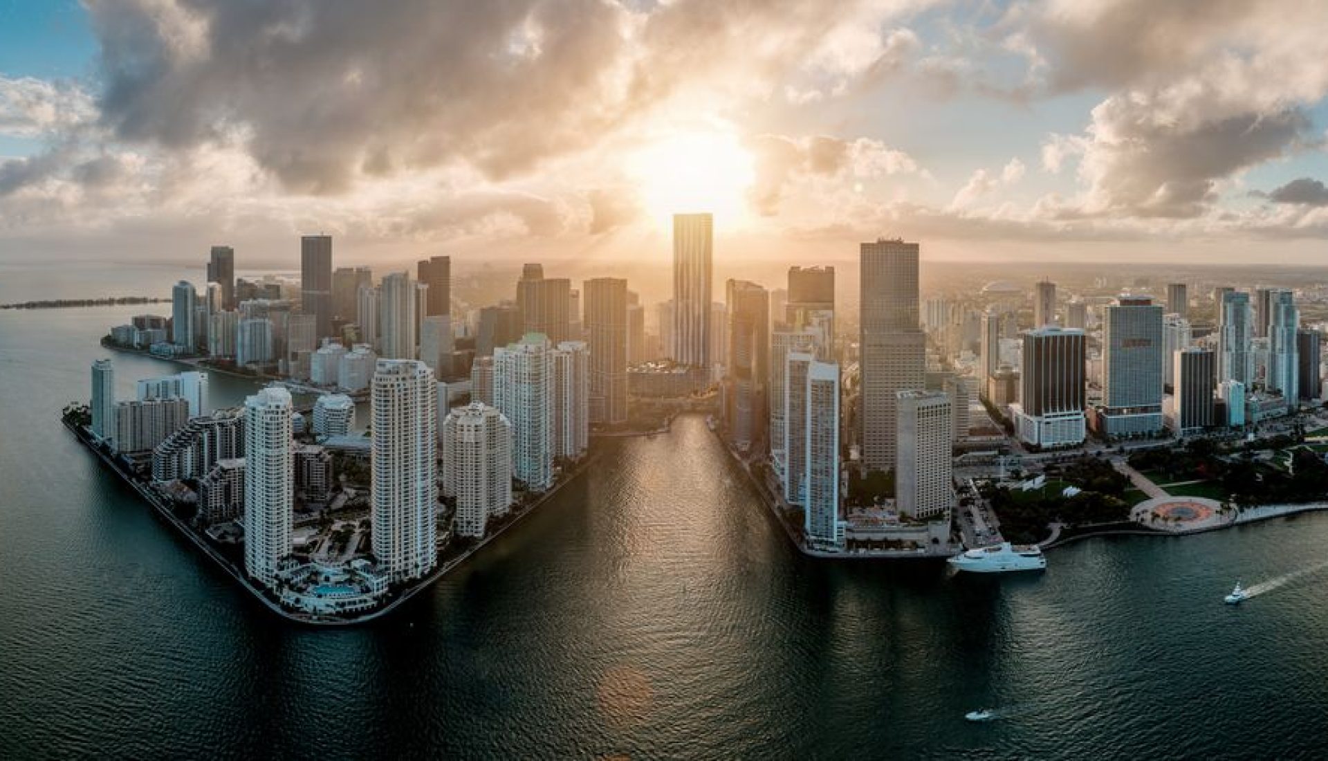 Aerial view of a coastal city skyline at sunset with high-rise buildings along a marina..