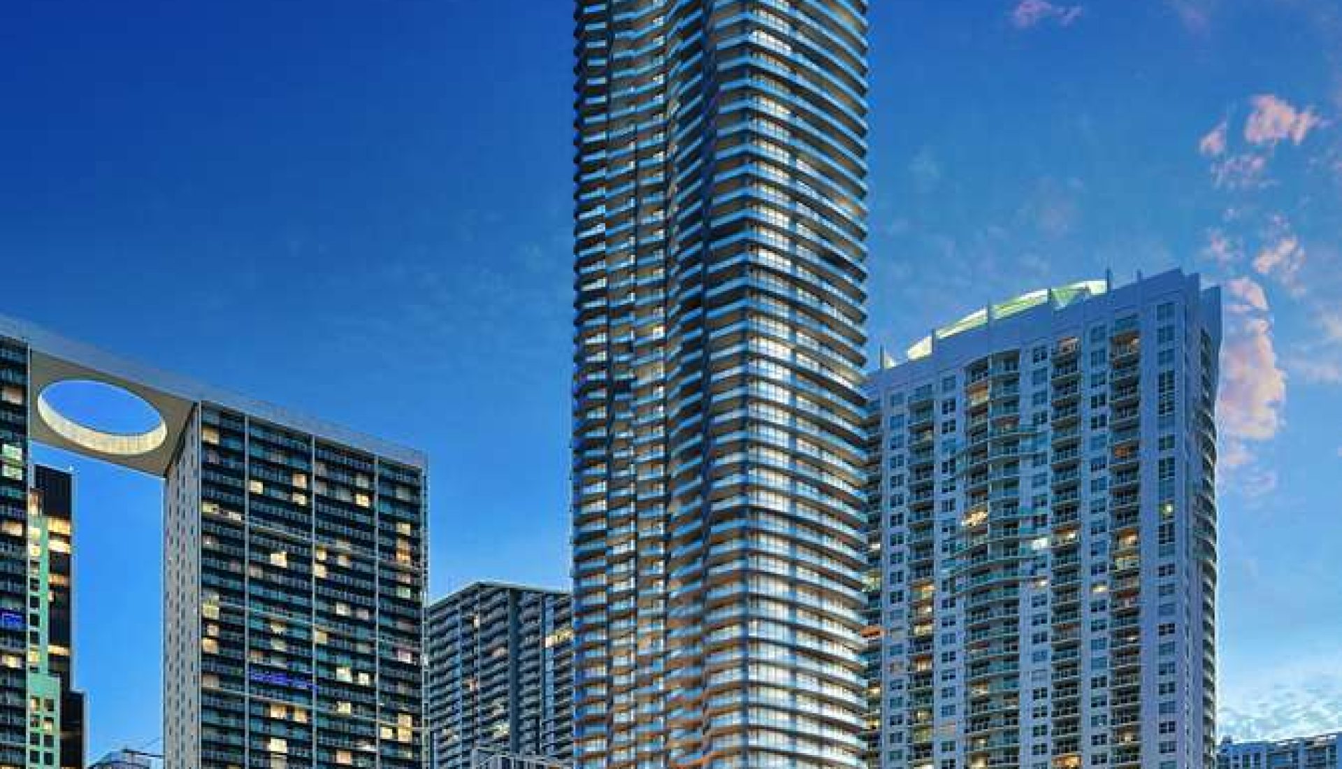 Tall glass skyscraper rises above a marina with luxury yachts under a deep blue evening sky.