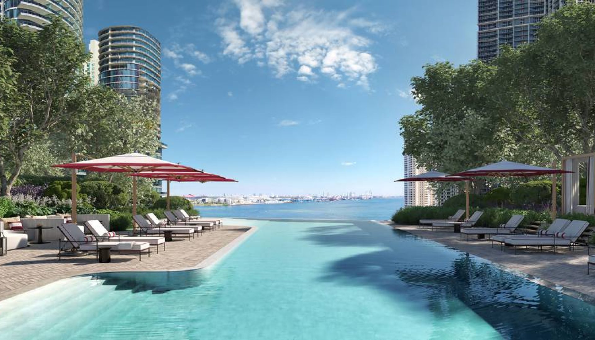 Luxurious pool deck with sun loungers under red umbrellas, facing a calm sea and city skyline beyond.