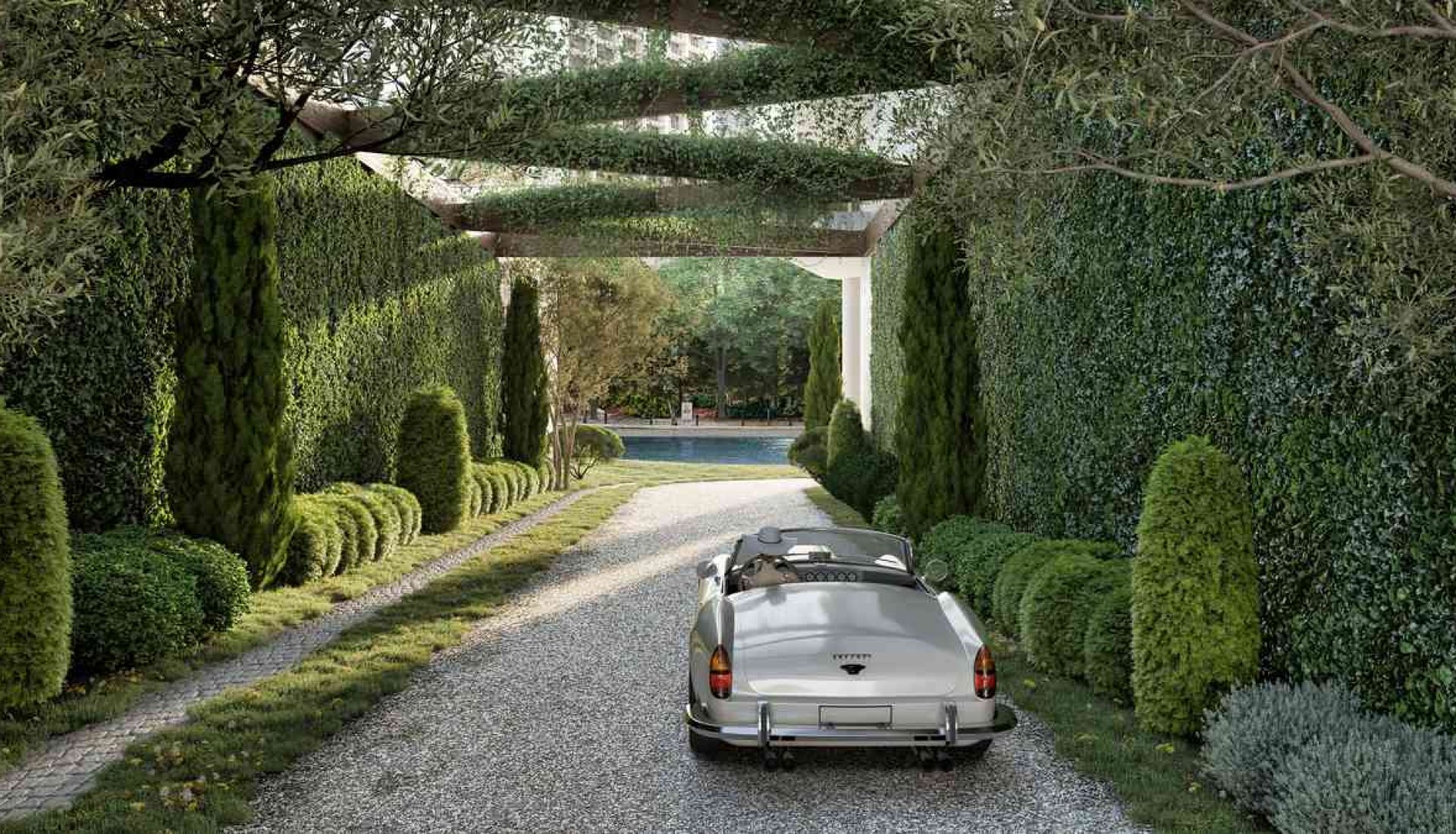 Silver vintage convertible parked on a gravel driveway under a trellis of greenery, leading to a formal garden and pool view behind the arches.