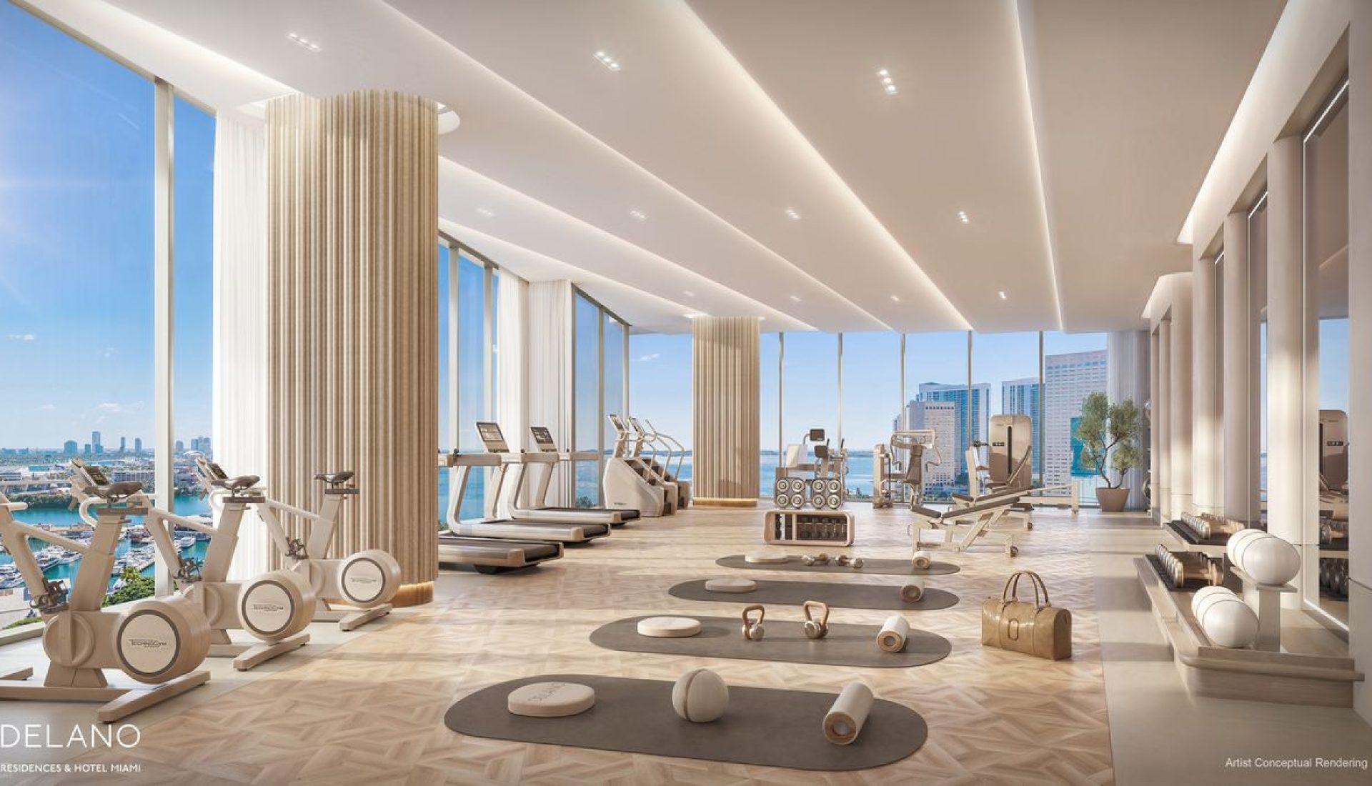 Bright luxury hotel gym with cardio machines by floor-to-ceiling windows and city views, plus free weights and mats on the floor centers of the room.