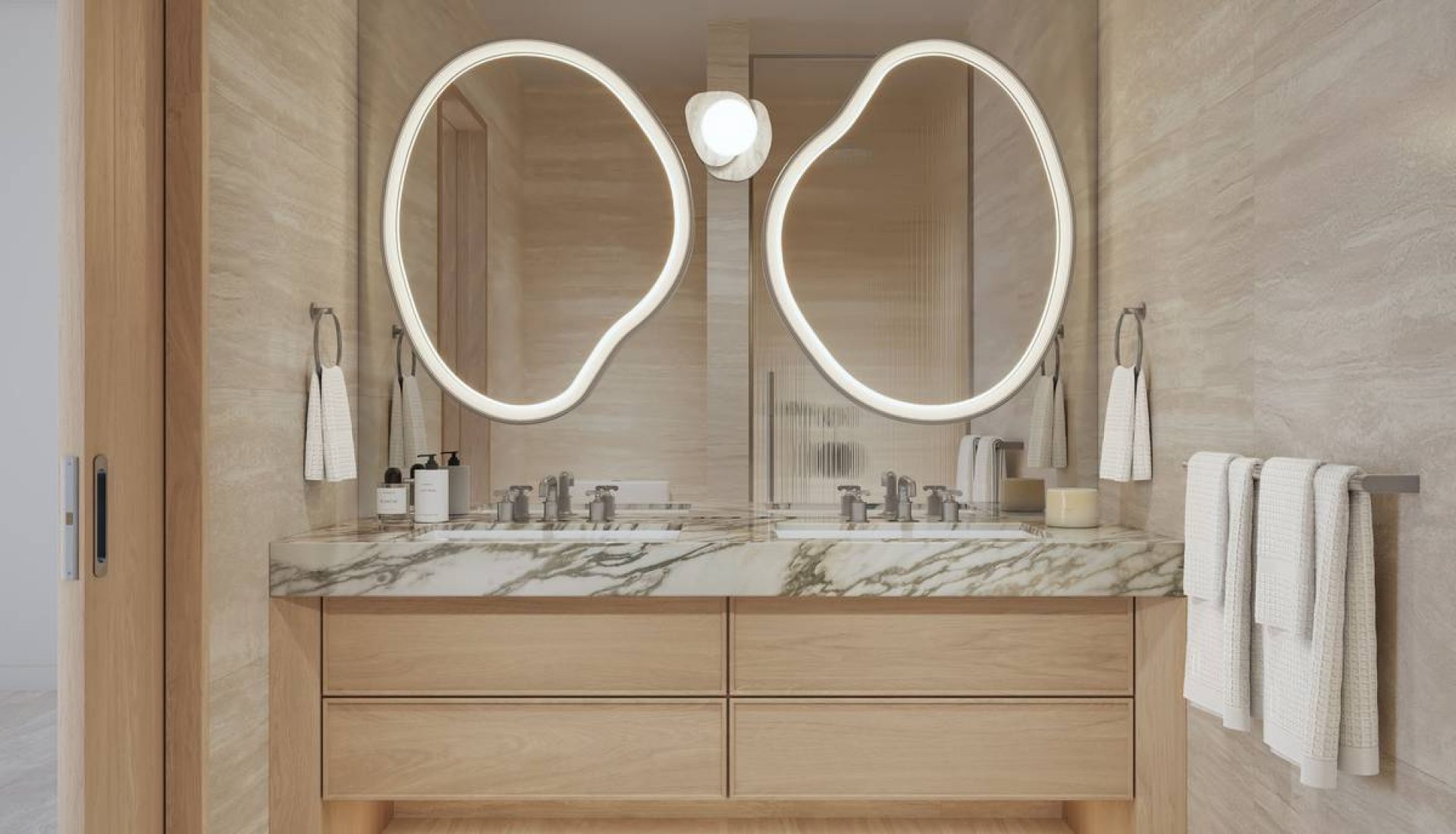 Double oval backlit mirrors above a marble countertop vanity in a beige-taupe bathroom with light wood cabinetry and towel racks nearby