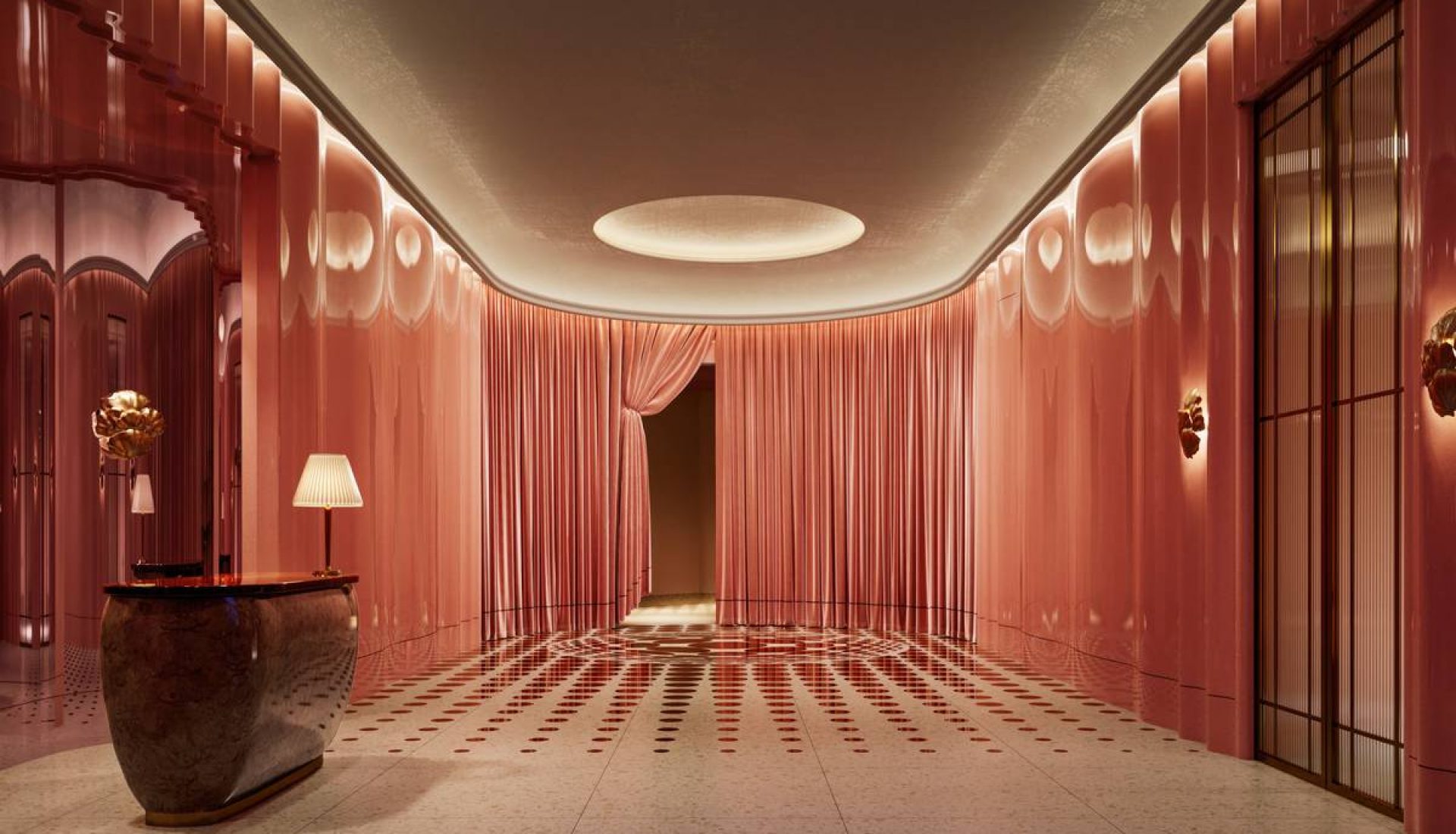 Luxurious pink hotel lobby hallway with curved ceiling, pink walls, and a marble reception desk with a lamp on the left.