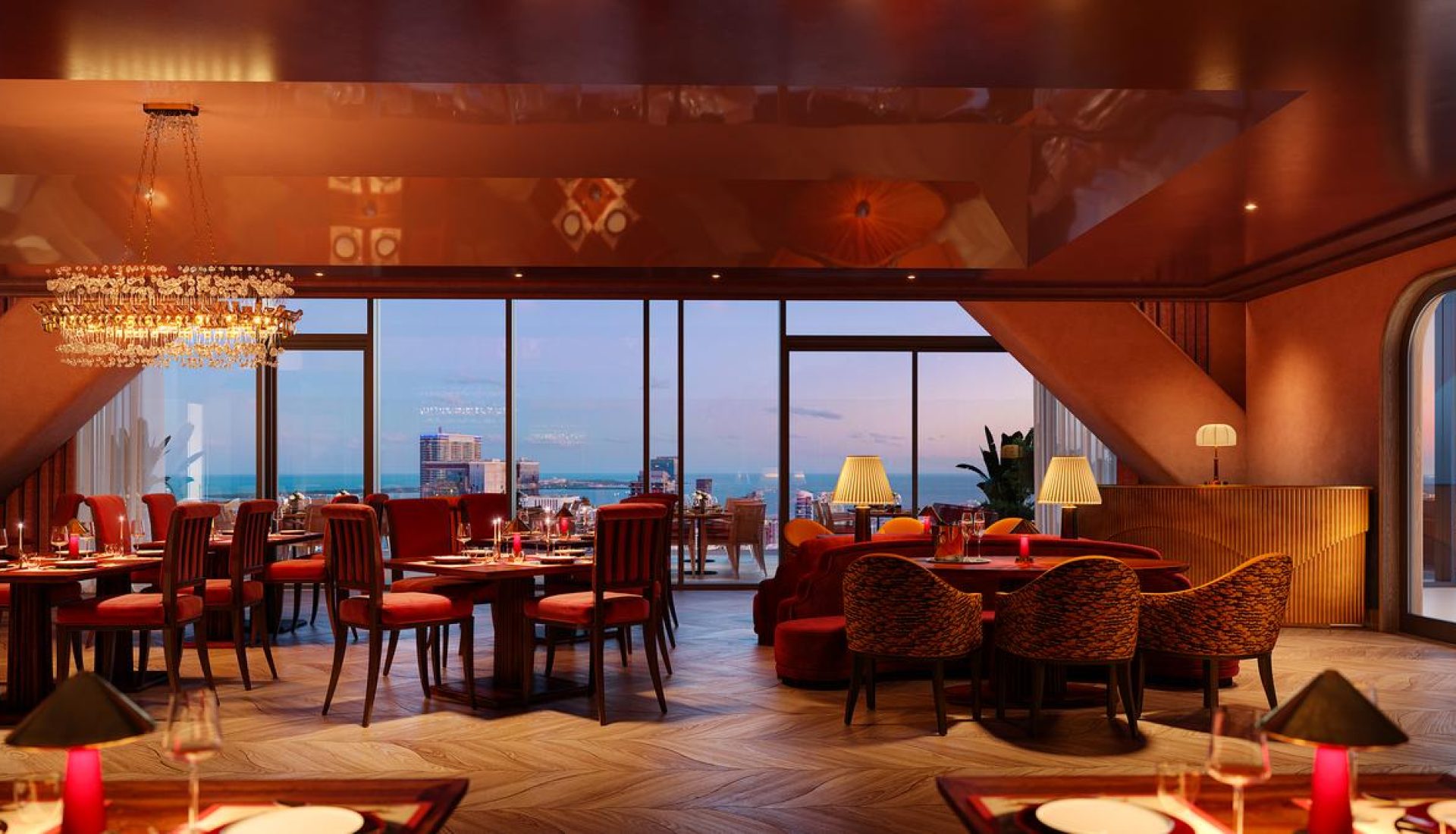 Upscale restaurant interior at sunset with red chairs, chandeliers, and large windows overlooking the city and ocean.