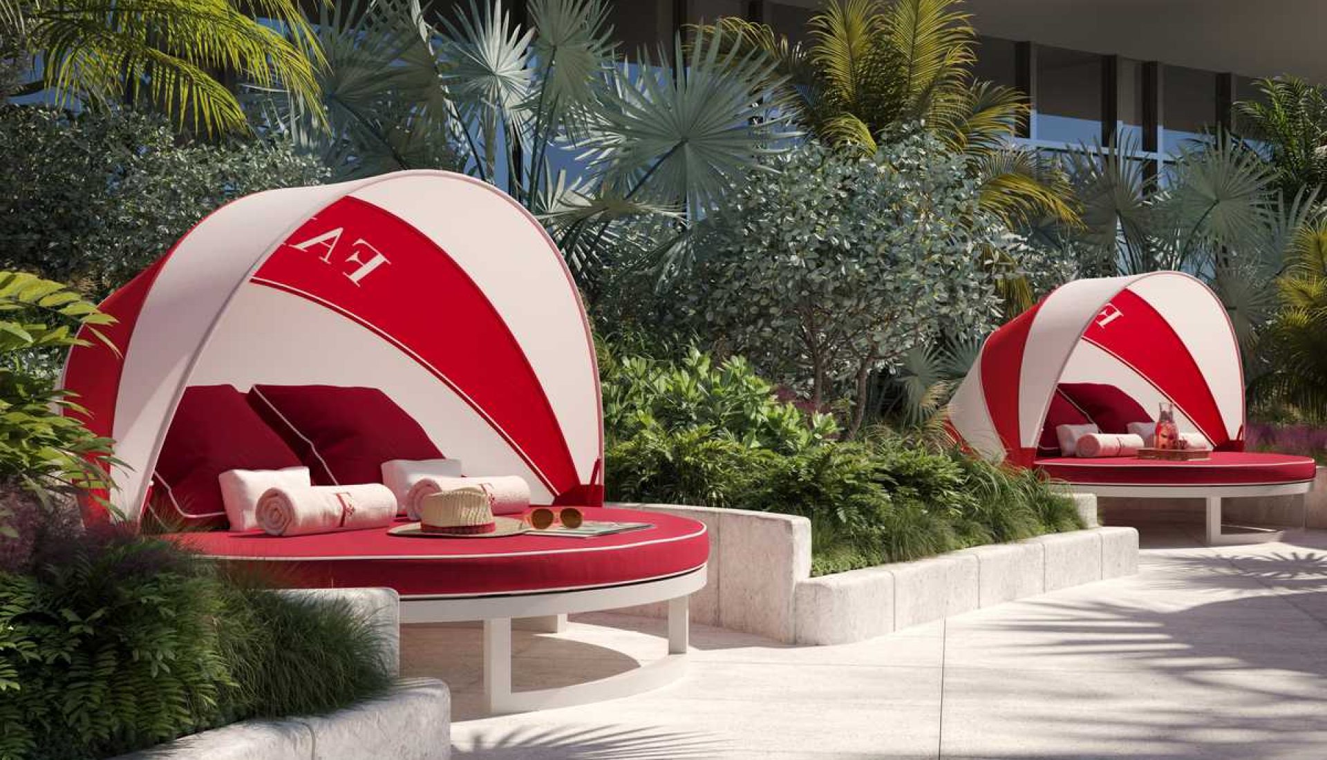 Two red-and-white outdoor cabana lounges with red cushions, towels, and a sun hat among lush tropical plants.