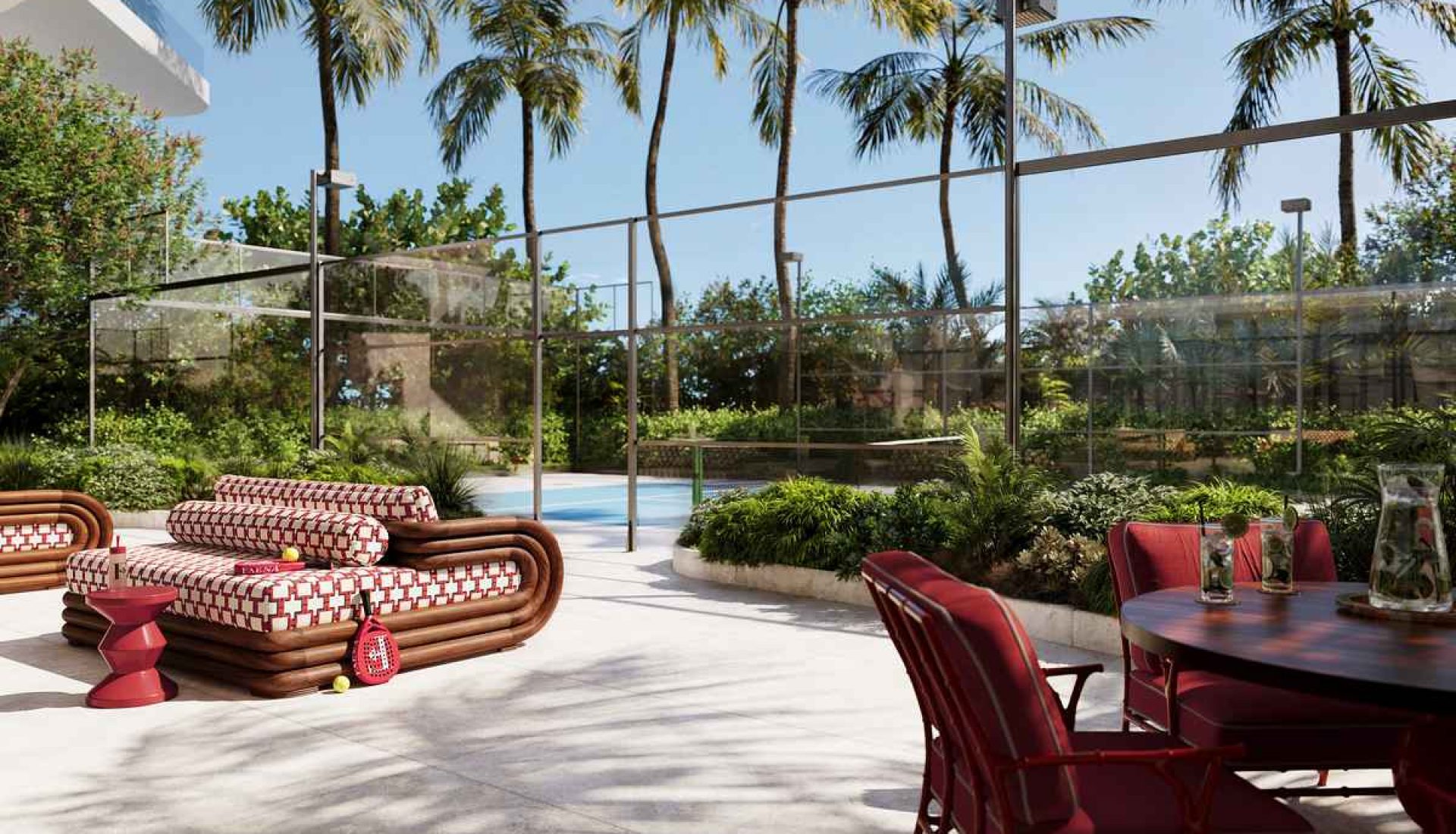 Uptown outdoor lounge area with red and patterned cushioned sofas beside a glass-walled pool under palm trees