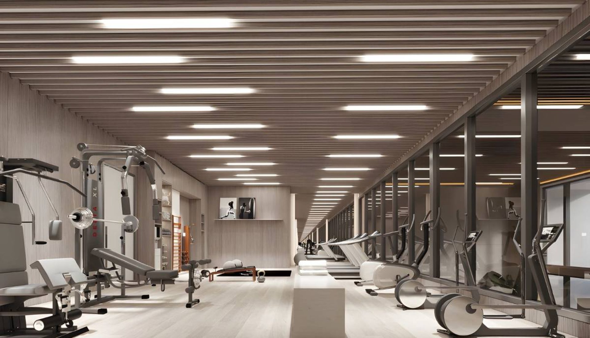 Modern gym interior with strength machines on the left and cardio machines along a glass wall on the right, under bright ceiling lights.