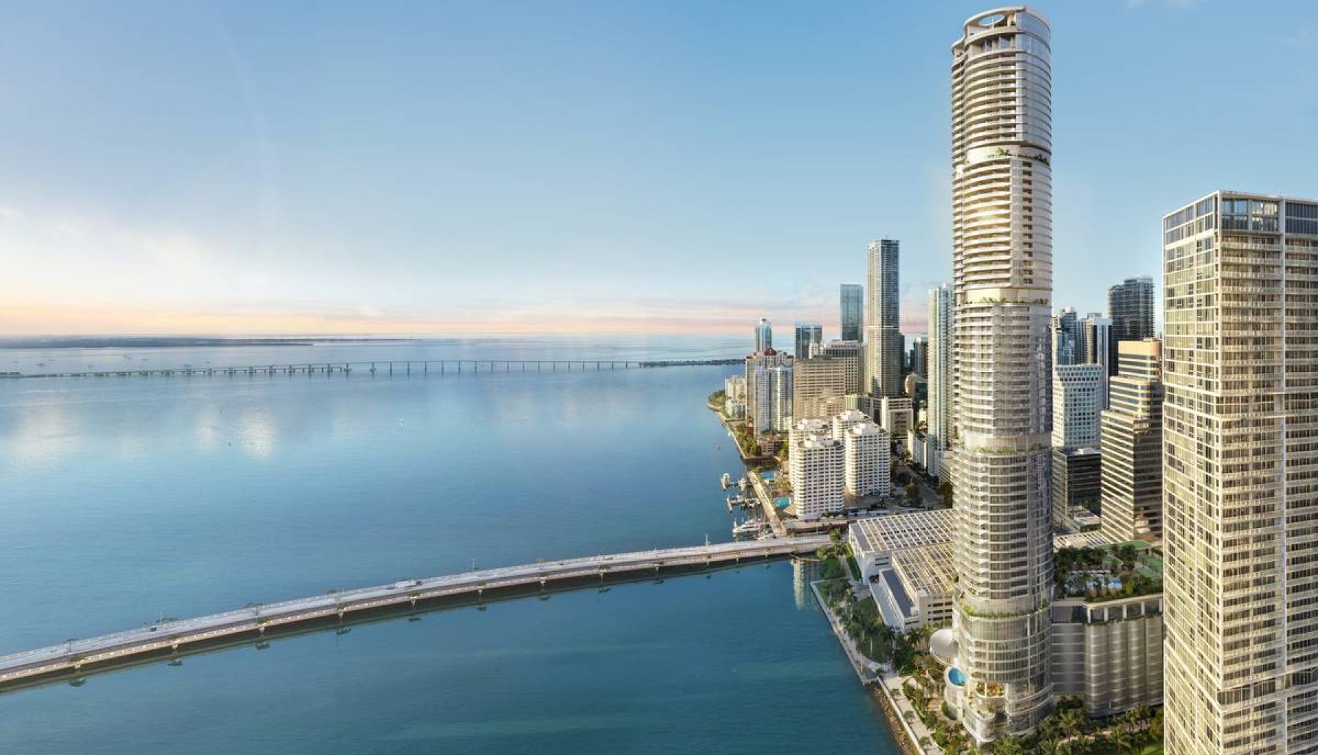 Aerial view of a coastal city with tall skyscrapers along a calm blue bay and a long pier extending into the water.