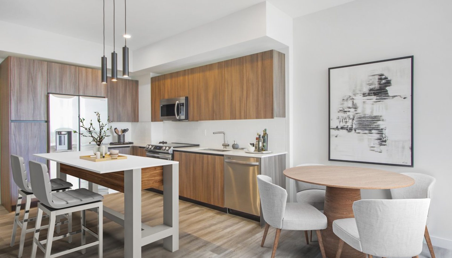 Modern open-concept kitchen with a white island, gray bar stools, wood cabinets, stainless appliances, and a round dining table with four chairs.