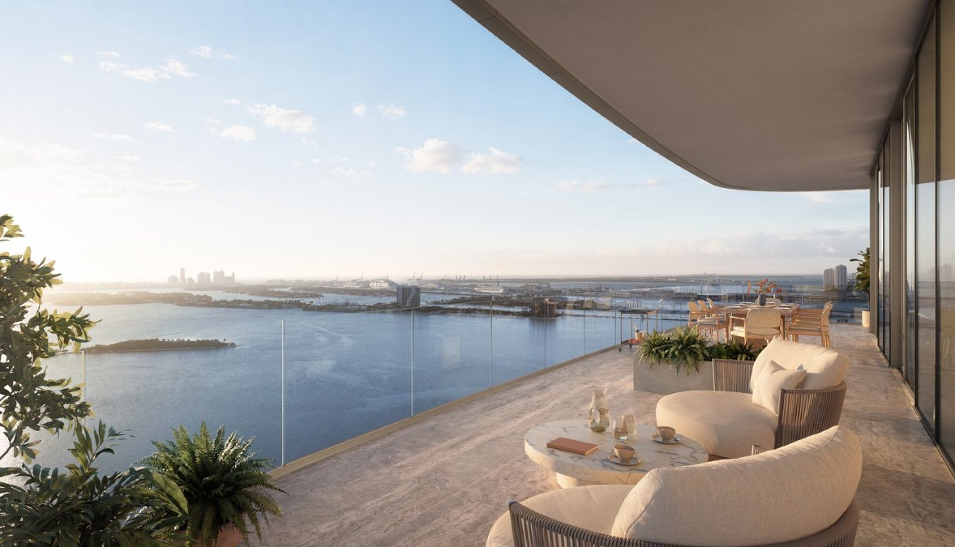 Rooftop terrace with curved cream couches and a marble coffee table, overlooking a blue bay and distant city skyline at sunset.
