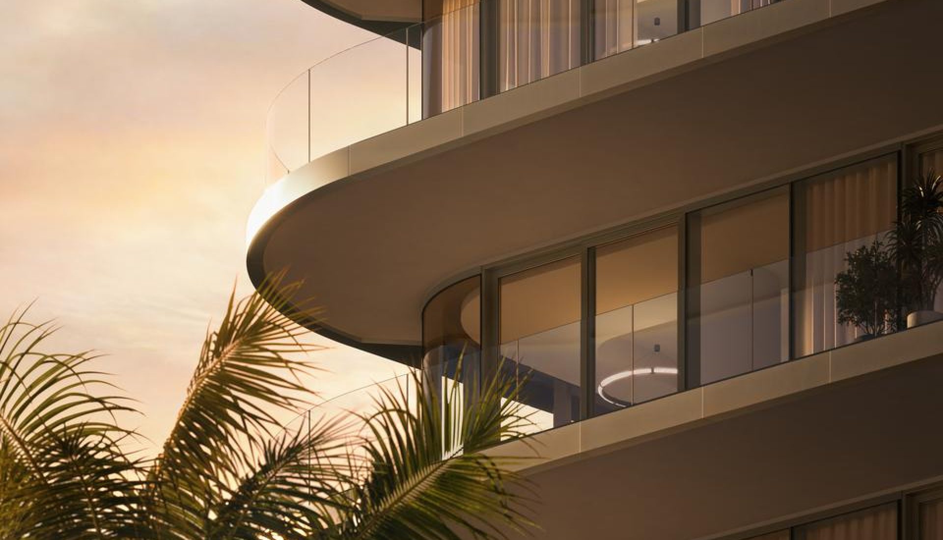 Curved glass balconies of a modern apartment building at sunset, with palm fronds in the foreground.