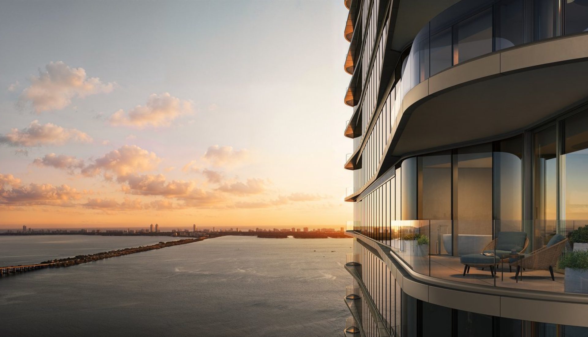Sunset over a calm bay seen from the curved glass balconies of a modern riverside building.