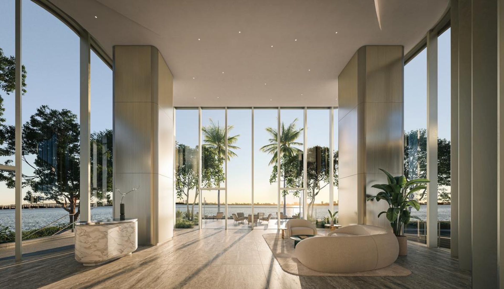 Modern hotel lobby with floor-to-ceiling glass walls, a water view, palm trees outside, and beige curved seating.