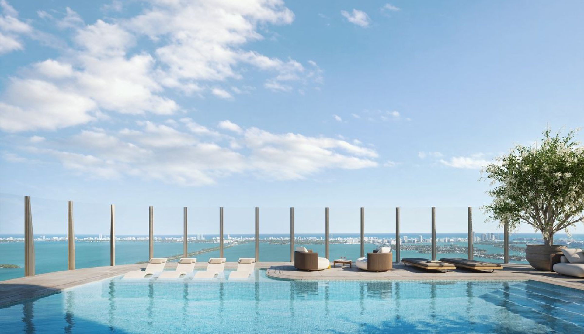 Rooftop infinity pool with white loungers and circular seating, glass barrier, overlooking the ocean and distant city skyline.