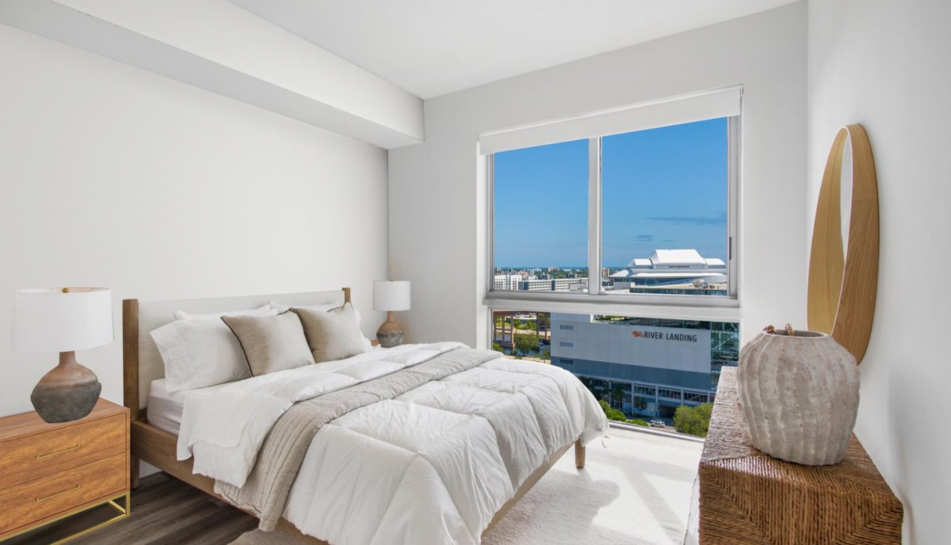 Bright, hotel-style bedroom with white bedding, beige pillows, and a large window with a cityscape view.