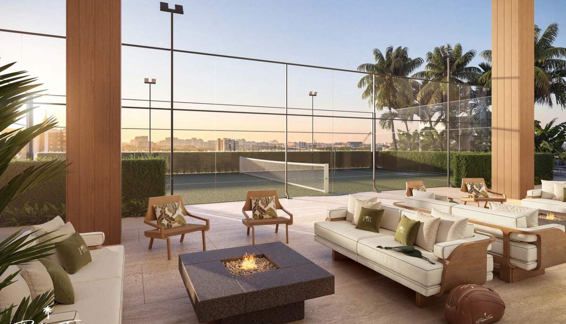 Luxurious rooftop outdoor lounge with a square fire pit, cream couches, and palm trees overlooking a city skyline at sunset.