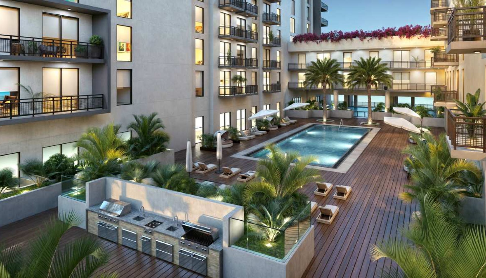 Courtyard pool area of a modern apartment complex with palm trees, lounge chairs, and grill stations.
