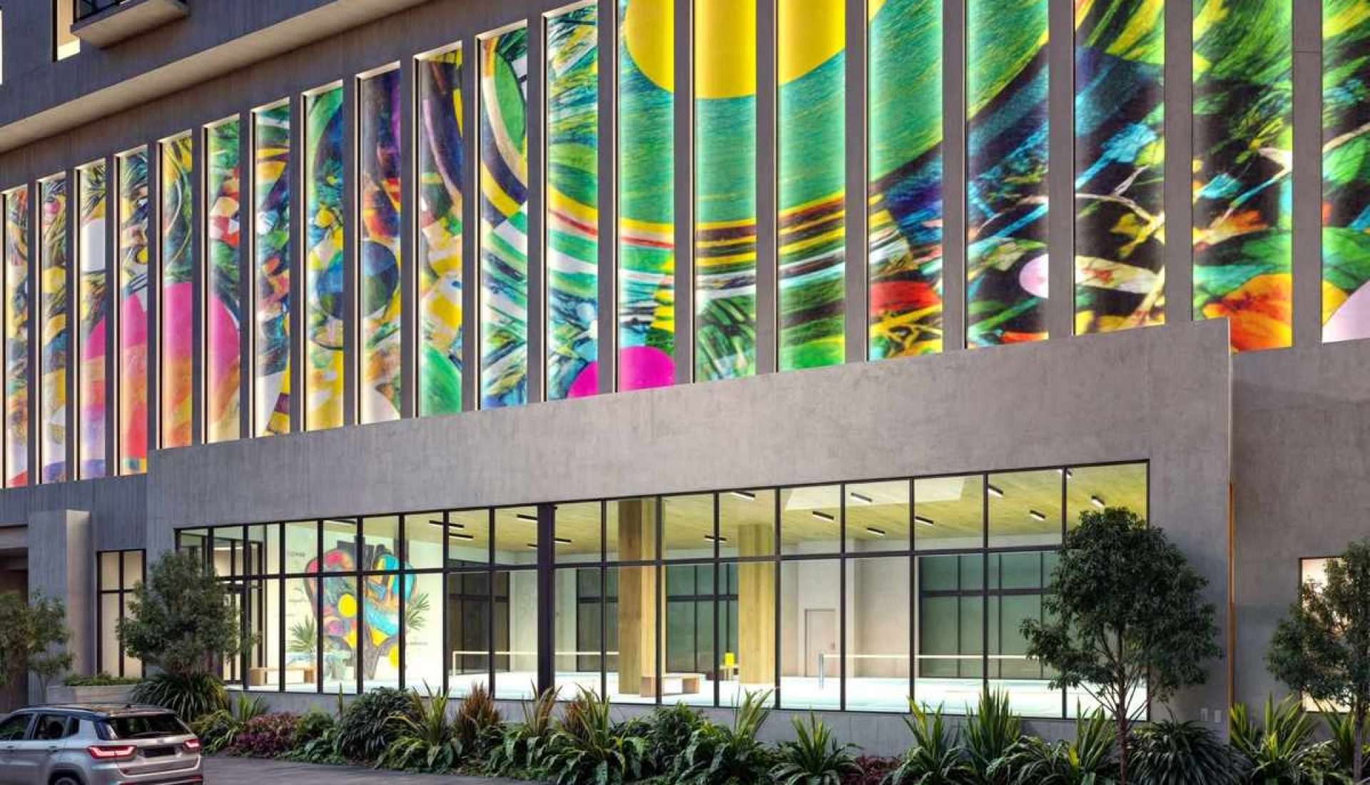 Modern building with tall colorful mural panels along the upper façade, glass storefront, and landscaped entry.