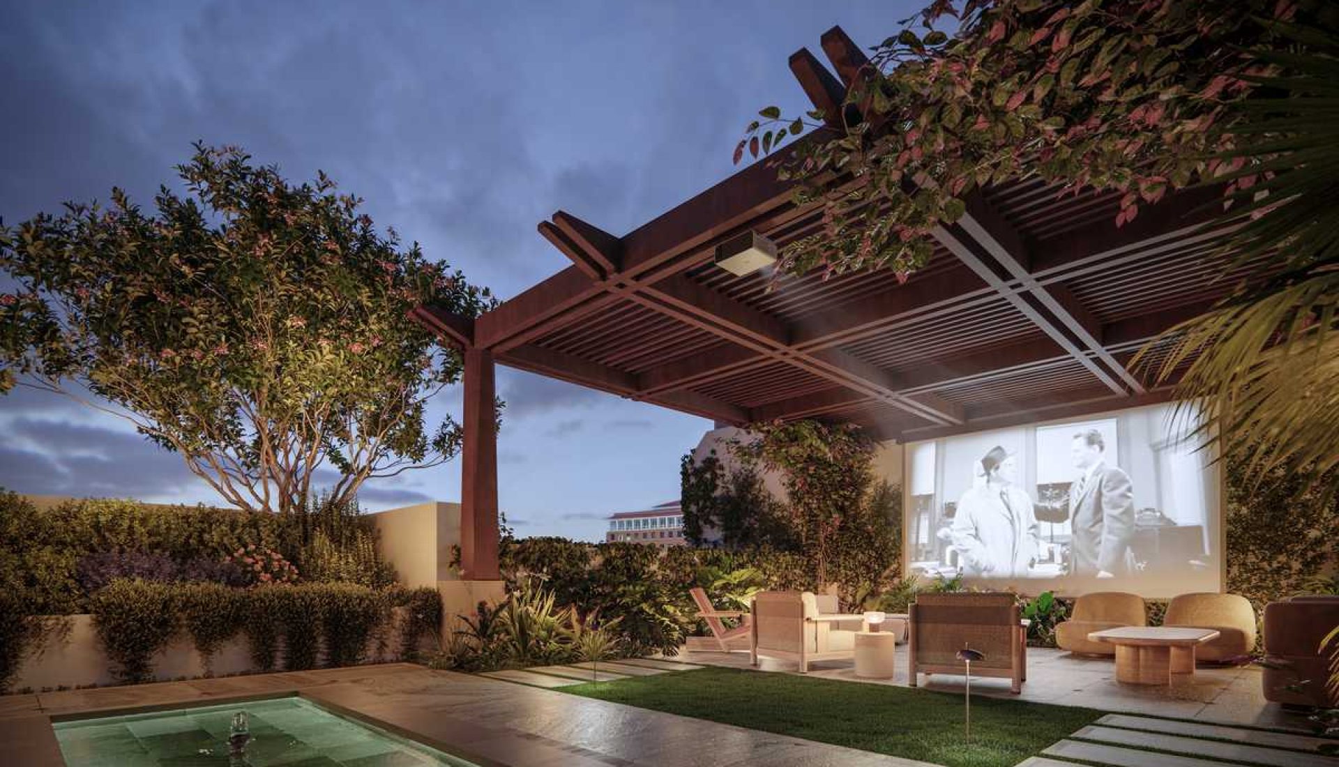 Outdoor home cinema under a wooden pergola with lounge seating, a projector screen showing a black-and-white film, and a rectangular pool nearby at dusk.
