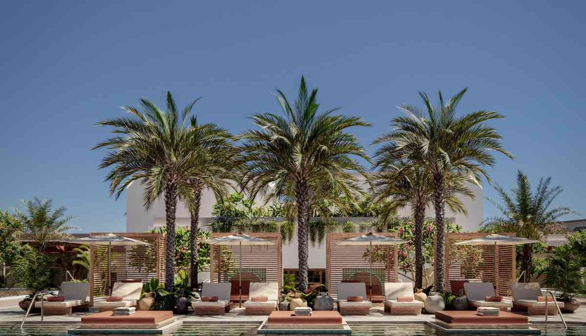 Poolside luxury resort with palm trees, cabanas, and sun loungers along a blue-tinted pool edge.