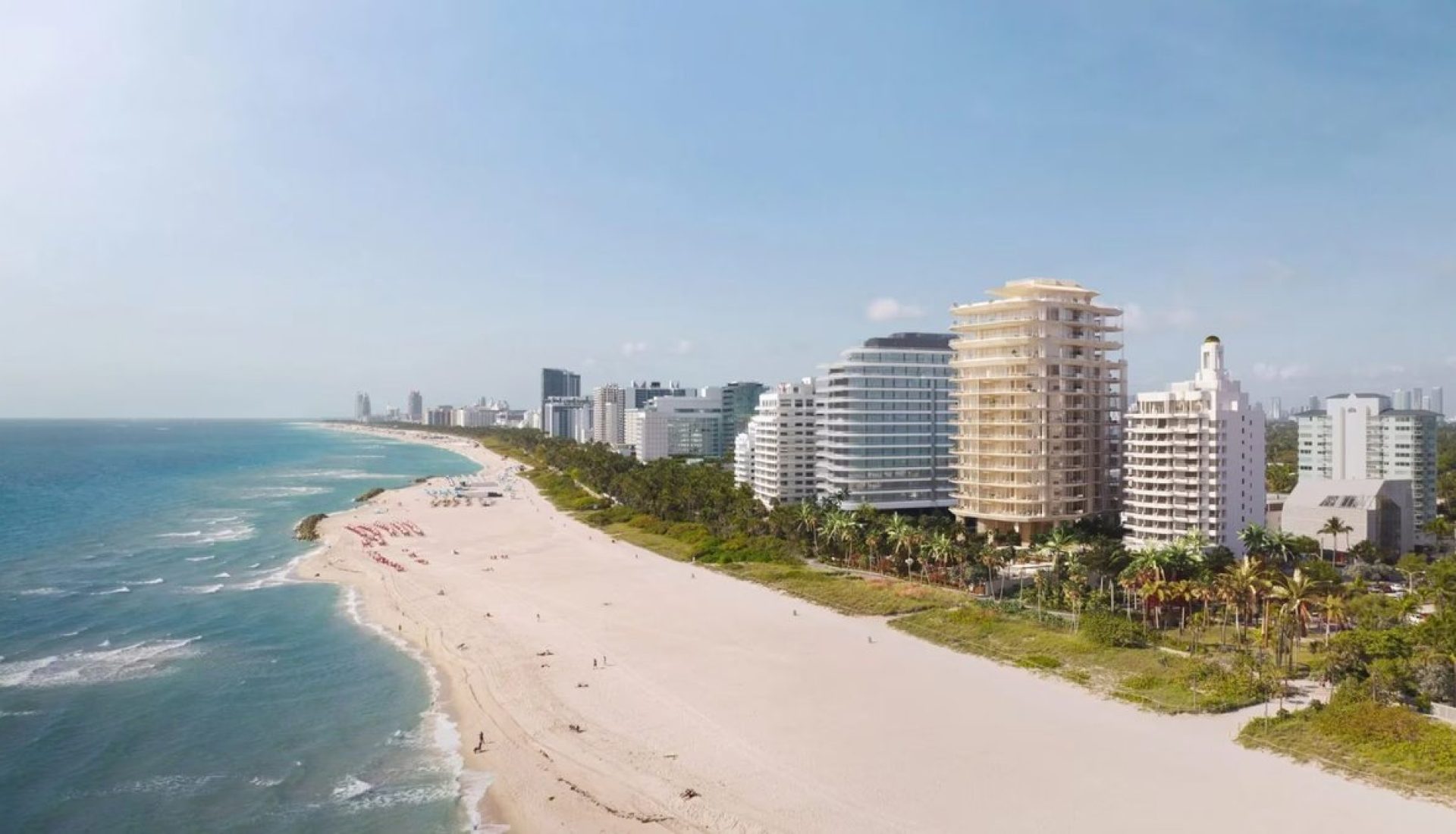 A sandy beach along a coastline with calm blue water and modern high-rise buildings lining the shore.
