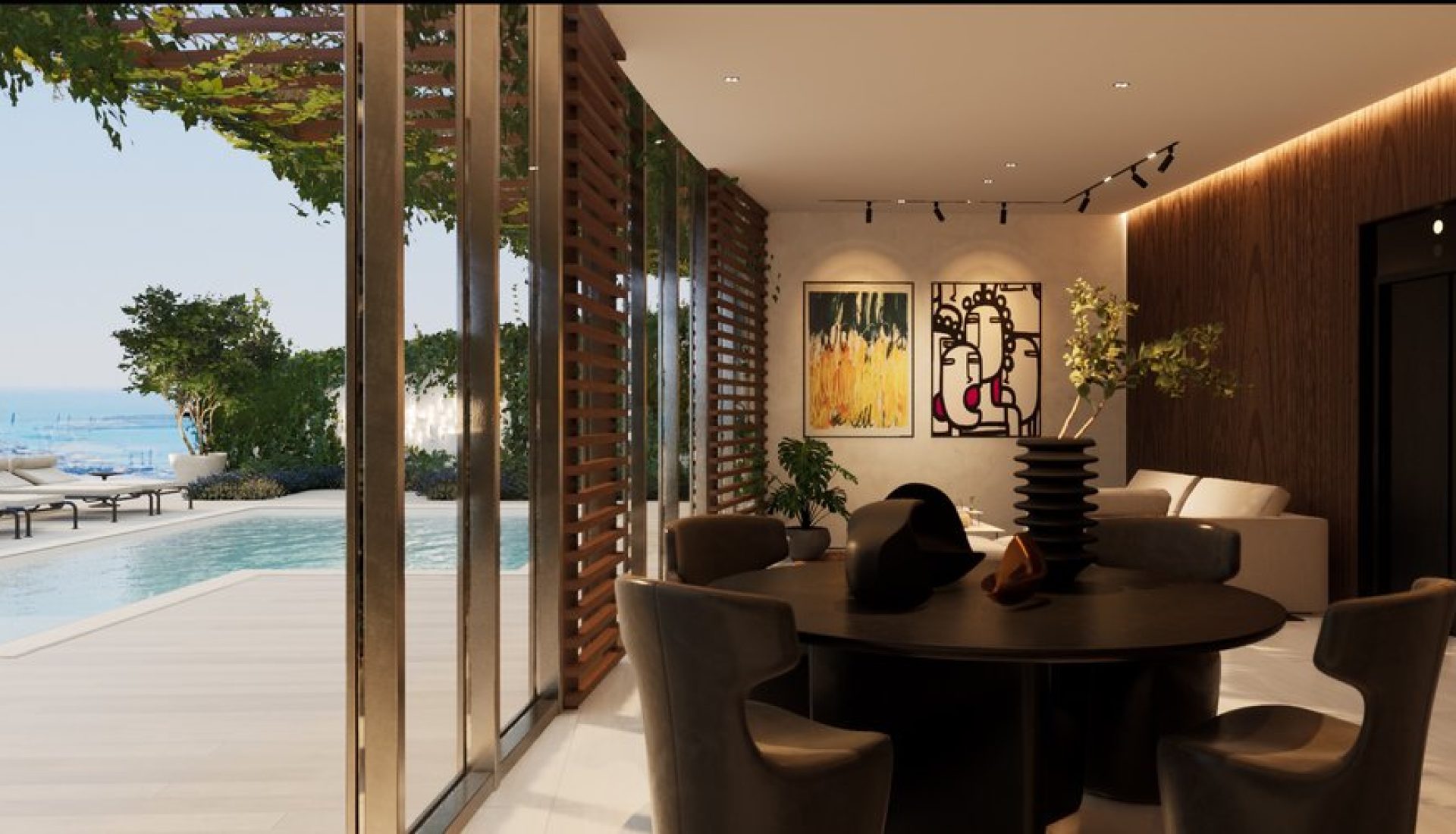 Interior dining area with a round black table and chairs, wood-paneled wall, and modern art, opening to a pool and ocean view outside.