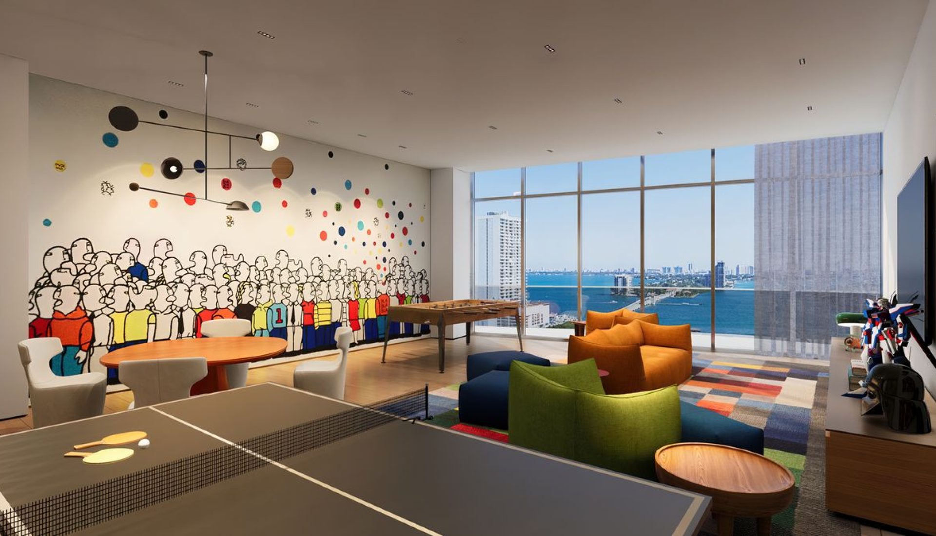 Bright recreation room with a crowd mural, round tables, white chairs, colorful seating, a foosball table, and large windows overlooking the water.