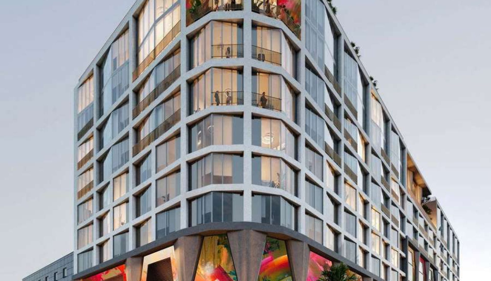 Modern multi-story building with large glass windows and colorful mural panels at ground level; people on balconies and pedestrians along the street.
